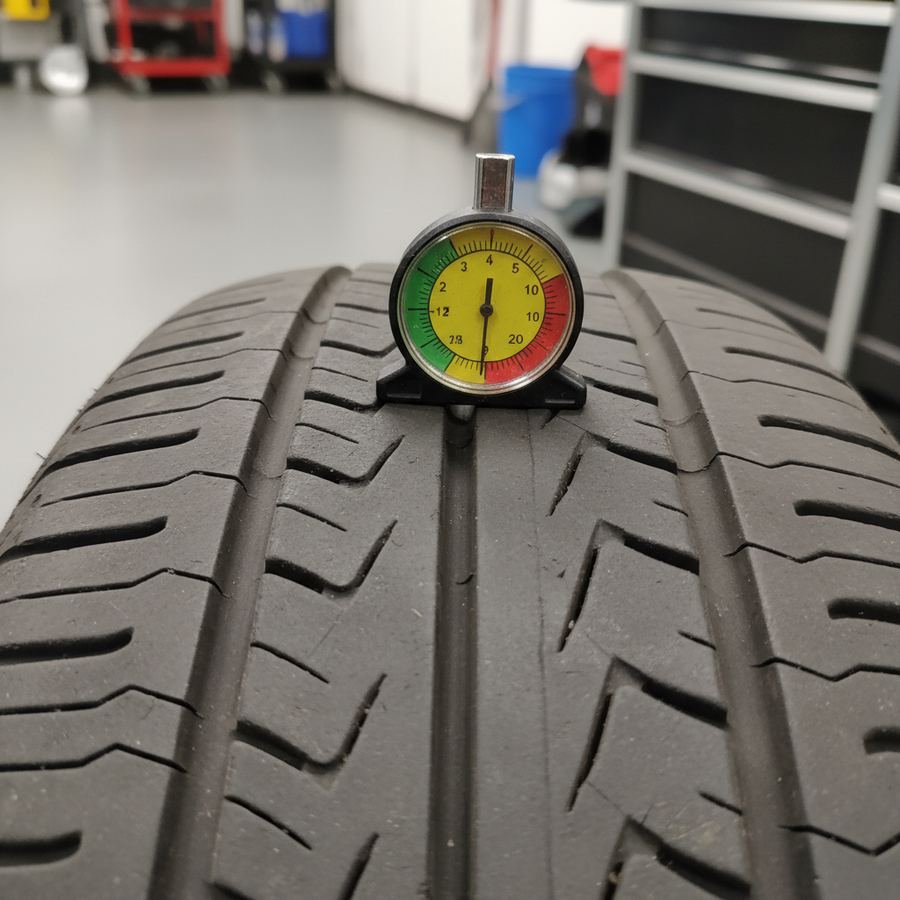 Mechanic measuring tire tread depth with a gauge on a worn tire